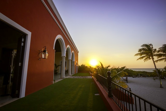 A stunning sunset casting a warm, golden glow over an elegant estate in Merida, Yucatan, reflecting the region's tranquil and luxurious lifestyle, ideal for a serene and upscale retirement