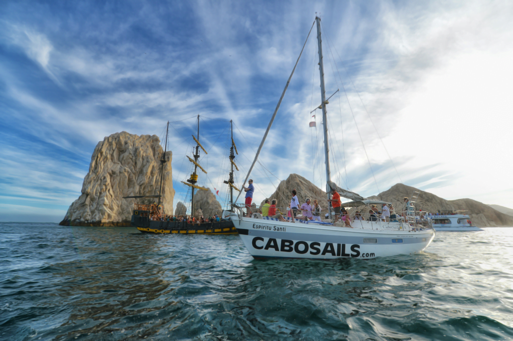 A serene sailboat navigating the calm, azure waters off the coast of Cabo San Lucas, with the striking rock formations in the background, offering a sense of peace and adventure, ideal for those seeking a tranquil yet exciting retirement by the sea.