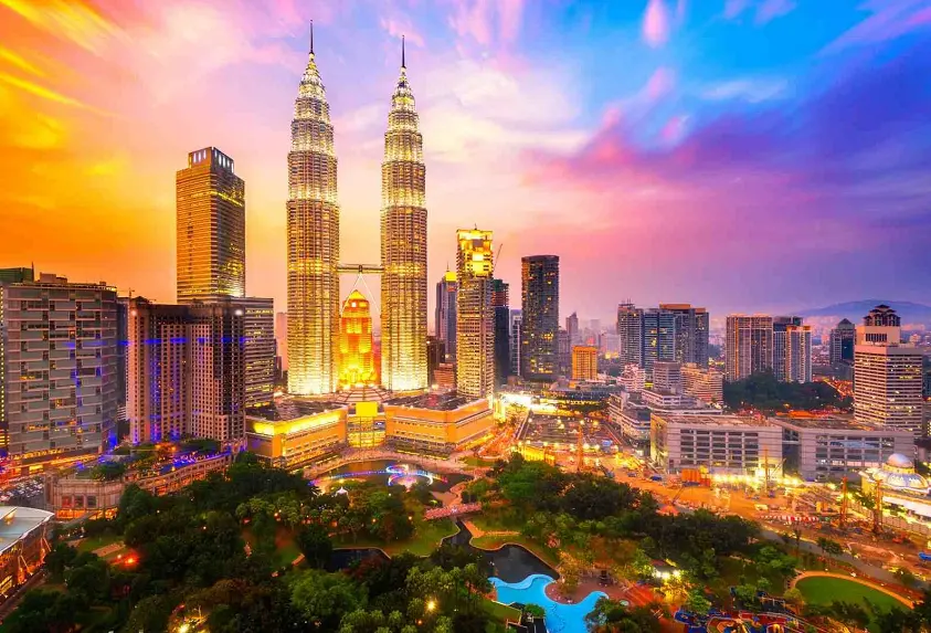 The Petronas Towers in Kuala Lumpur, Malaysia, illuminated at night, standing tall against the city skyline with a connecting skybridge between the two towers.